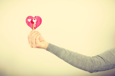 Key to happiness and living together. Love and dream. Woman hand holds little red heart with keys to...