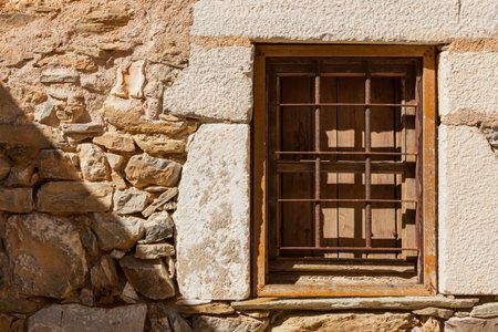 Old wooden window with chutters and metal grilles in old stone wall made building home.