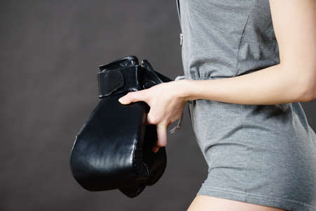 Unrecognizable sporty woman holding black boxing gloves after fight. Studio shot on dark background.の写真素材