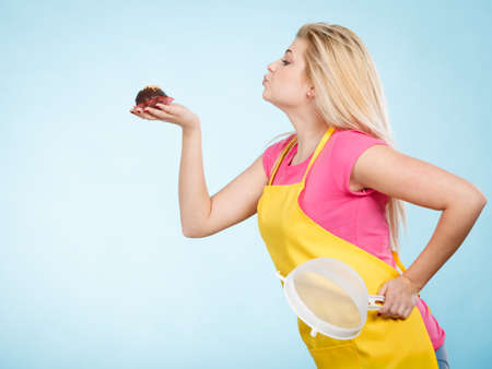 Baking tasty desserts sweets at home concept. Blonde woman holding delicious chocolate cupcake and colanderの写真素材