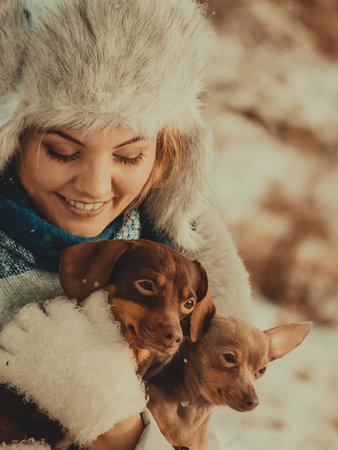 Young woman having fun outside in snow. Female playing with her small purebreed dogs puppies in cold...