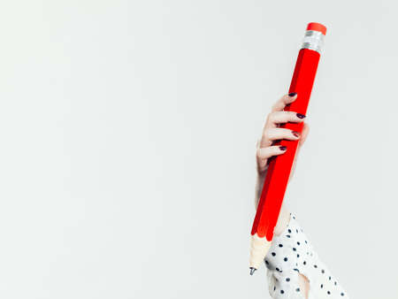 Education, stationery elements, school concept. Female hand student girl or business woman female teacher holding big red pencil. Studio shot on greyの写真素材