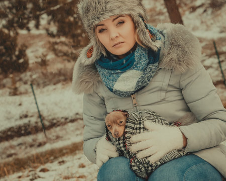 Young sad woman wrapped her best friend little dog in warm blanket scarf to warm him in cold winter day. Animal protection save. Adoption conceptの写真素材