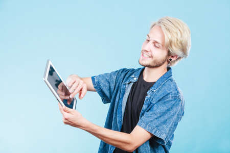 Education social media. Modern technology internet concept. Stylish handsome young guy using tablet computer, on blue colorの写真素材