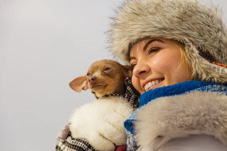 Young woman wrapped her best friend little dog in warm blanket scarf to warm him in cold winter day....