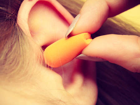 Woman putting ear plugs into her ears getting rid on noise in loud place.の写真素材