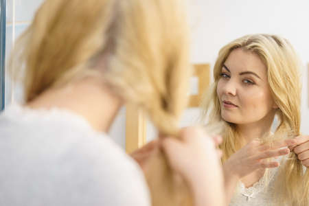 Young pretty blonde woman creating her hairstyle, making braid. Lovely female getting readyの写真素材