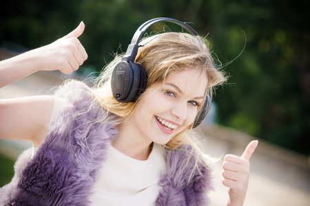 Happy joyful woman listening to music while being outdoor. Teenage female wearing headphones having...