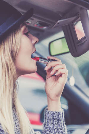 Young attractive woman looking in rear view mirror painting her lips doing applying make up while driving the car.の写真素材