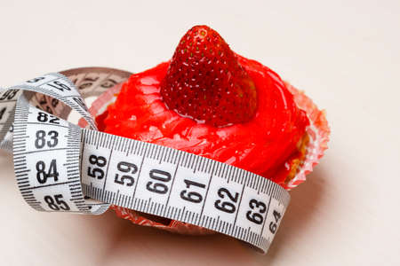 Appetite and gluttony concept. Fattening problem. Cake cupcake with measuring tape on tableの写真素材