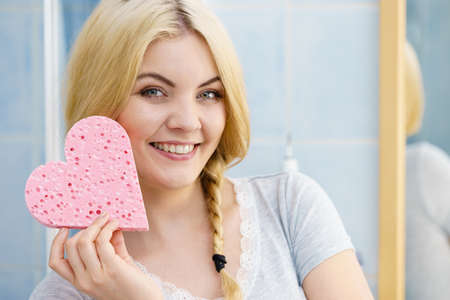 Young pretty adorable woman having two cute braids on blonde hair holding pink sponge in heart shape. Haircare and hairstyling concept.の写真素材