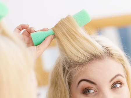 Blonde woman using hair rollers to create beautiful hairstyle on her hairdo.の写真素材