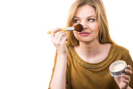 Fashionable cheerful young female holding professional powder brush, adding last touch to her make...