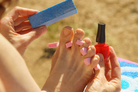Unrecognizable woman doing pedicure during vacations outdoor on beach. Female buffing her foot nails...