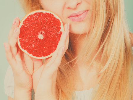 Woman positive girl holding half of red grapefruit citrus fruit in hands near mouth. Healthy diet food. Summer holidays concept. Toned imageの写真素材