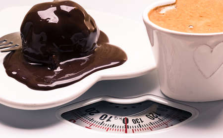 Cup of coffee and chocolate cake on heart shaped plate saucer on weighing scale. Unhealthy nutrition. Fat diet concept.の写真素材