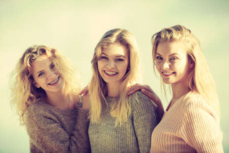 Three fashionable women wearing sweaters during warm autumnal weather spending their free time in park. Fashion models outdoorの写真素材