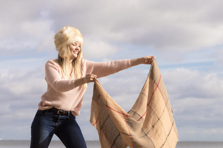 Teenage female spending time outdoor on the beach during autumn weather. Wearing sweater, scarf and...