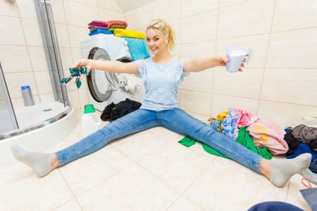 Woman in bathroom doing laundry, choosing the best detergent. Female holding powder container and gel pods for washing clothes. Household duties. Wide angle viewの写真素材