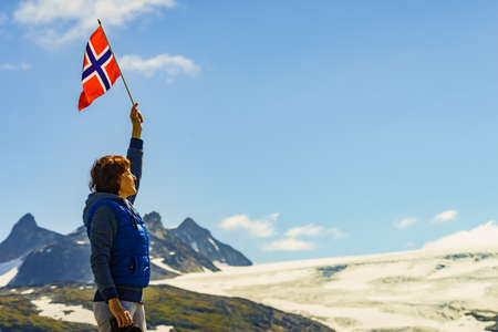 Tourist woman enjoy mountains landscape, holding norwegian flag. National tourist scenic route 55 Sognefjellet, Norwayの写真素材
