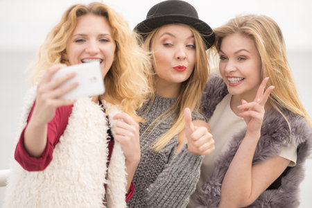 Three females taking selfies, having fun outdoor using smart phone to take photo.