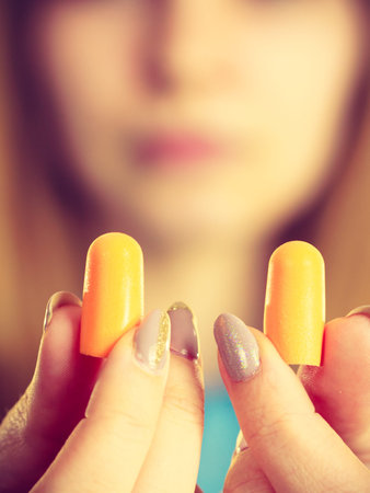 Woman holding protective ear plugs. Getting rid on noise in loud place, hearing protection concept.