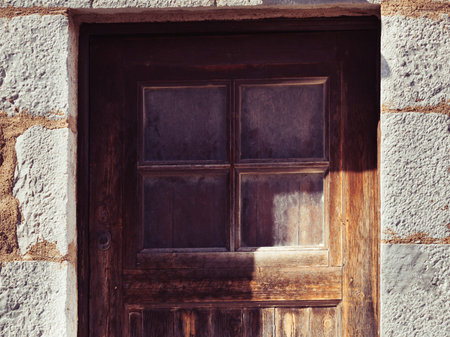 Old brown wooden made door with little window in ancient aged building made of stoens.