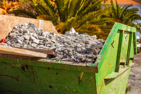 Green metal container with construction waste rubble for disposal. Heavy garbage on construction siteの写真素材