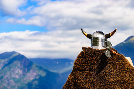 Viking warrior with helmet and axe on fjord shore in Norway. Tourism and traveling concept
