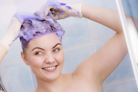 Woman applying coloring shampoo on her hair. Female having purple washing product. Toning blonde color at home.の写真素材