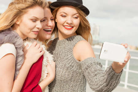 Three females taking selfies, having fun outdoor using smart phone to take photo.の写真素材