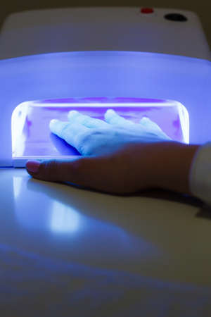 Woman hand in uv led lamp drying gel hybrid manicure on nails. Beauty wellness spa treatment concept.の写真素材