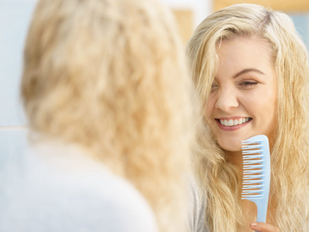 Blonde woman getting ready in bathroom before going out, brushing her hair having fun and singing to...
