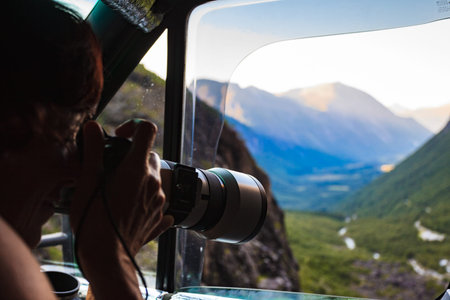 Mature woman tourist professional photographer taking photo from camper car with camera, driving on...