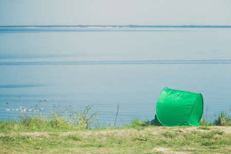 Tourism and recreation. Small green tent in natural area surrounded by meadow water sea lake.の写真素材