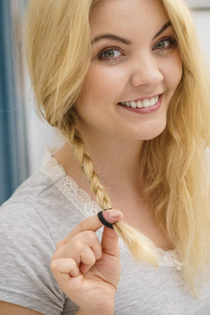 Young pretty blonde woman creating her hairstyle, making braid. Lovely female getting ready