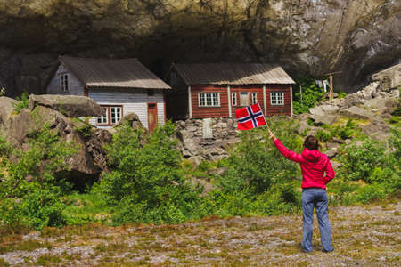 Tourist woman visiting the Helleren houses in Jossingfjord along road 44 between Egersund and Flekkefjord, Female holding norwegian flag. Sokndal municipality, Norway.