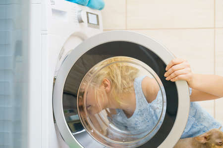 Woman looking inside of washing machine doors. Investigating laundry utensil in bathroom.の写真素材