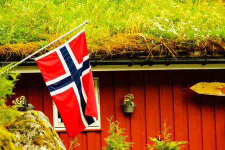 The norwegian flag waving against typical red country house with grass on the roofの写真素材