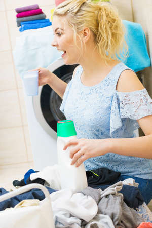 Young woman sitting in bathroom sorting clothes into washing machine. Female doing dark laundry holding liquid and powder detergent.の写真素材
