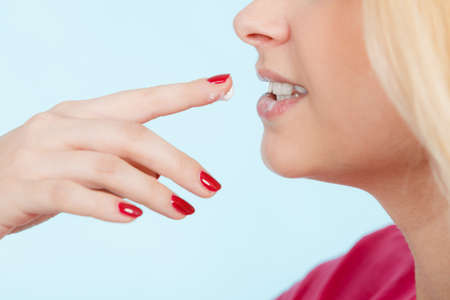Diet, sweets temptation, delicious food concept. Woman licking whipped cream from finger or applying lip balm to dry lips, presenting her red nailsの写真素材