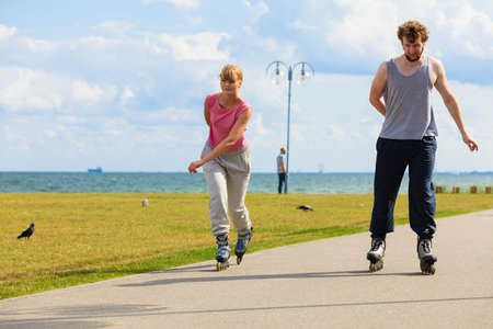 Love romance leisure outdoor fitness sport concept. Young pair riding rollerskates in park. Girl and boy together on skates.の写真素材