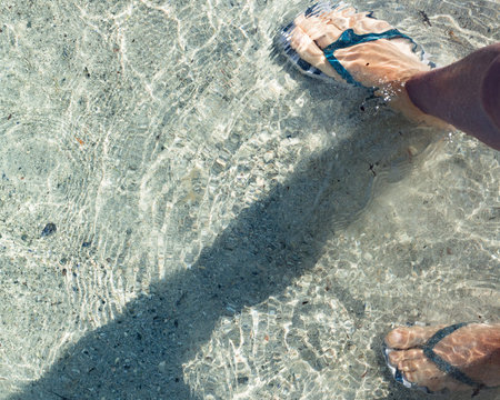 Female's feet in flip flop shoes on sandy beach. Summertime.