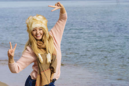 Teenage female spending time outdoor on the beach during autumn weather. Wearing sweater, scarf and fur hat.の写真素材