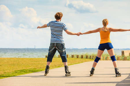 Holidays, active people and friendship concept. Young fit couple on roller skates riding outdoors on sea coast, woman and man rollerblading together on the promenadeの写真素材