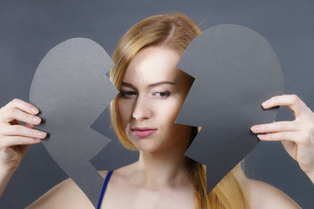 Depression, sadness, relationship problem concept. Young female with broken heart full of negative sad emotions. Woman covering her face by two parts of black love symbol.の写真素材