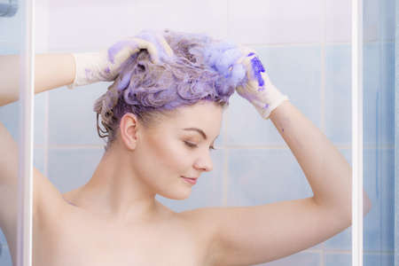 Woman applying coloring shampoo on her hair. Female having purple washing product. Toning blonde color at home.の写真素材