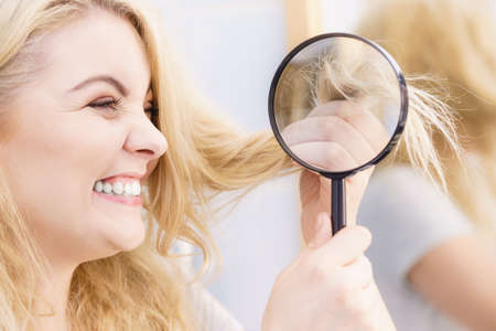 Happy woman magnifying her hair ends looking through magnifier being positive about conditioner results on her hairdos.の写真素材