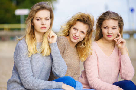 Three fashionable women wearing sweaters during warm autumnal weather spending their free time on sunny beach. Fashion models outdoorの写真素材