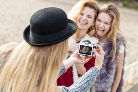 Three females friends having fun during outdoor photo session. Woman taking pictures of two during warm autumn weather.の写真素材